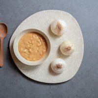 Zuppa di cipolle con cucchiaio in legno e tre cipolle bianche intere